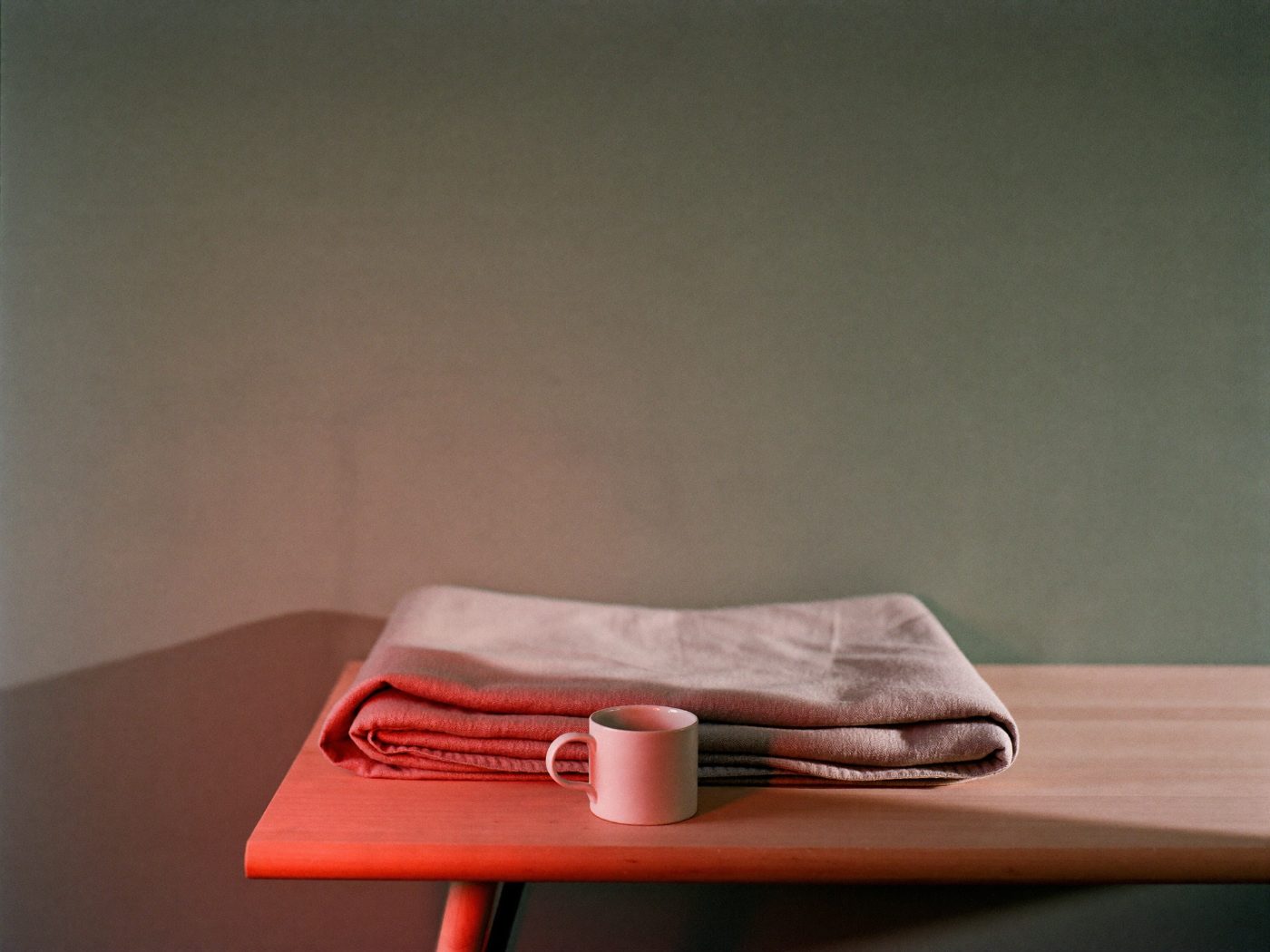 A folded linen throw and a ceramic mug on a bench, with red light falling across the surface